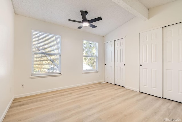 unfurnished bedroom with ceiling fan, lofted ceiling with beams, light hardwood / wood-style floors, a textured ceiling, and two closets