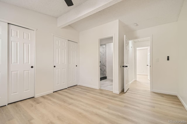 unfurnished bedroom with beam ceiling, a textured ceiling, light hardwood / wood-style floors, and two closets