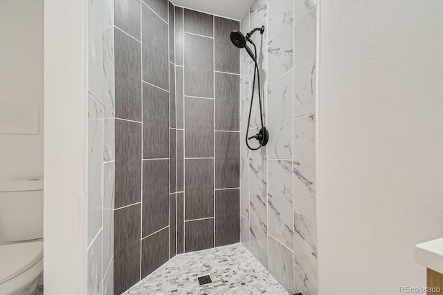 bathroom with a tile shower and toilet