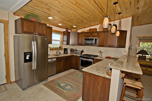 kitchen with hanging light fixtures, light stone countertops, stainless steel appliances, sink, and a kitchen bar