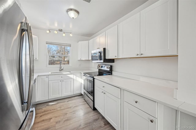 kitchen featuring light wood-type flooring, appliances with stainless steel finishes, sink, and white cabinets