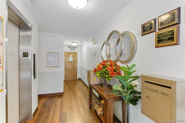 hall featuring wood-type flooring, a textured ceiling, and elevator