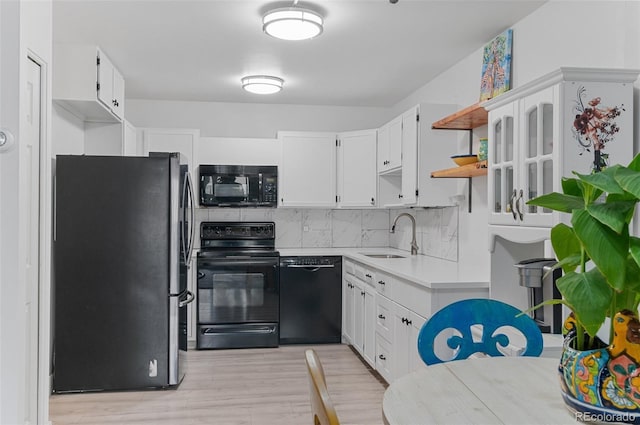 kitchen featuring a sink, black appliances, light wood finished floors, decorative backsplash, and light countertops