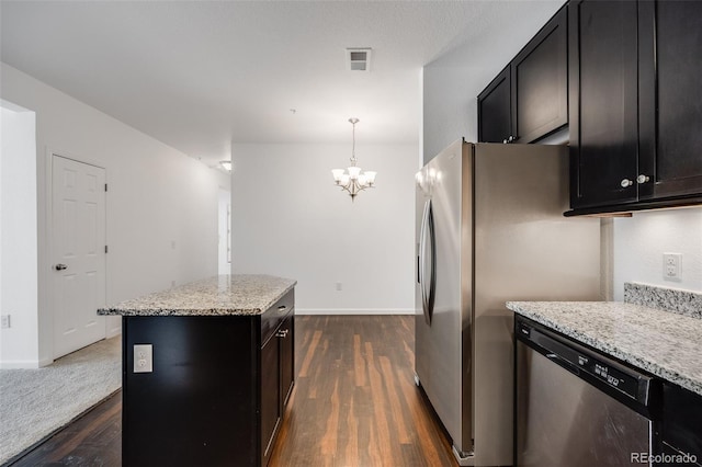 kitchen featuring dark wood-type flooring, appliances with stainless steel finishes, hanging light fixtures, light stone countertops, and a kitchen island