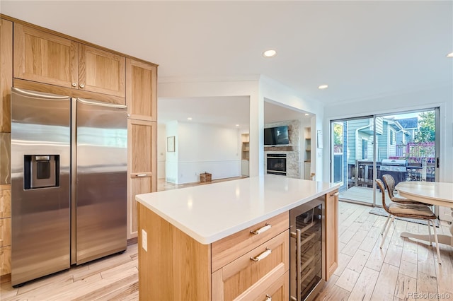 kitchen featuring a stone fireplace, light hardwood / wood-style flooring, wine cooler, built in refrigerator, and a center island