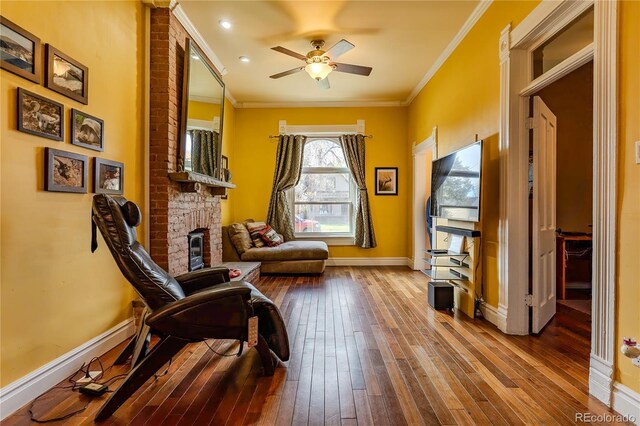 living area featuring baseboards, ornamental molding, wood-type flooring, and a ceiling fan