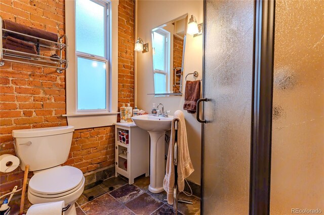 bathroom featuring a shower stall, toilet, brick wall, and stone tile floors