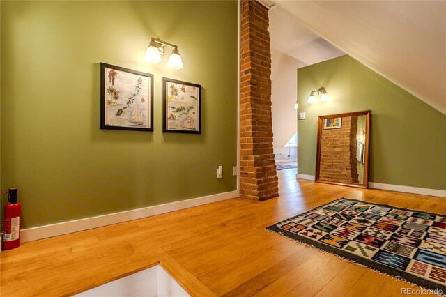 interior space with ornate columns, baseboards, wood finished floors, and lofted ceiling