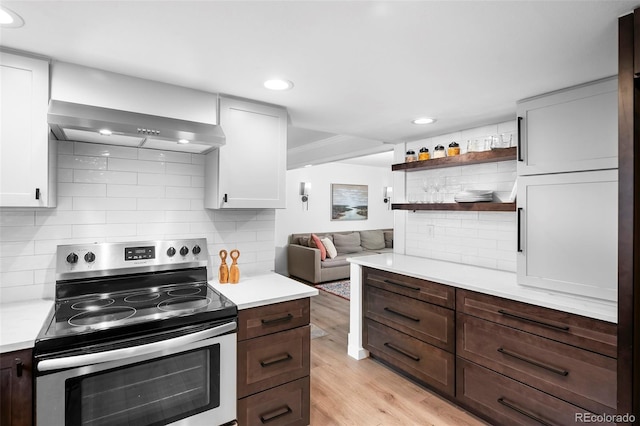 kitchen with white cabinets, electric range, wall chimney exhaust hood, light wood-type flooring, and tasteful backsplash