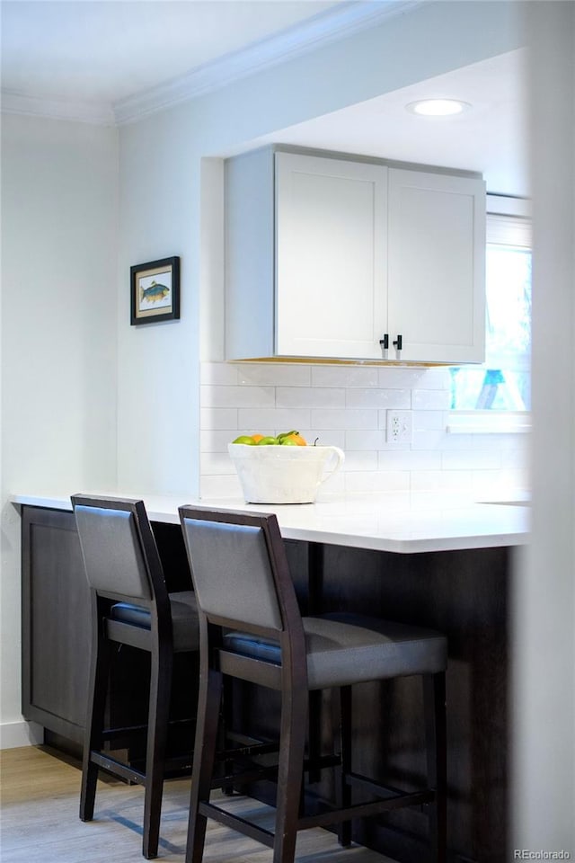 bar with backsplash, crown molding, and light wood-type flooring