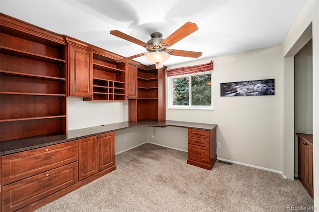 unfurnished office featuring light carpet, built in desk, and ceiling fan