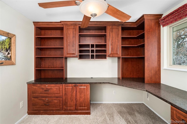 unfurnished office featuring ceiling fan, built in desk, and light carpet