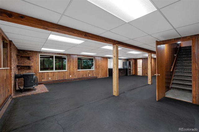 3 Twilight Dr, Wheat Ridge, CO 80215 - basement with a wood stove, a baseboard heating unit, a paneled ceiling, wooden walls, and stairs