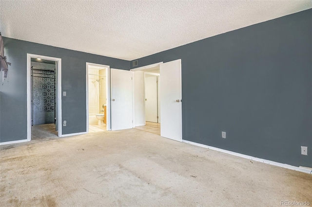 unfurnished bedroom with carpet, a textured ceiling, connected bathroom, and baseboards