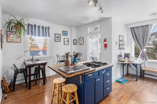 kitchen featuring a kitchen bar, stainless steel gas cooktop, dark wood-type flooring, and blue cabinets