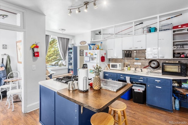 kitchen with white appliances, backsplash, white cabinets, light wood-type flooring, and blue cabinetry