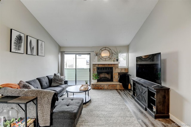 living room with baseboards, a stone fireplace, lofted ceiling, and light wood-type flooring