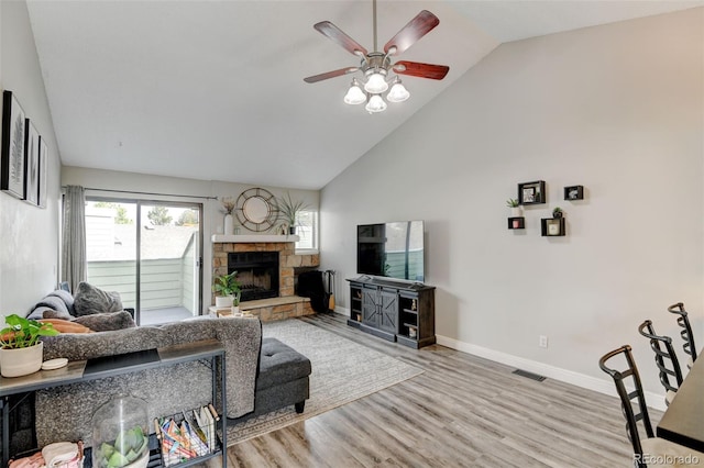 living room featuring a ceiling fan, a stone fireplace, visible vents, wood finished floors, and baseboards