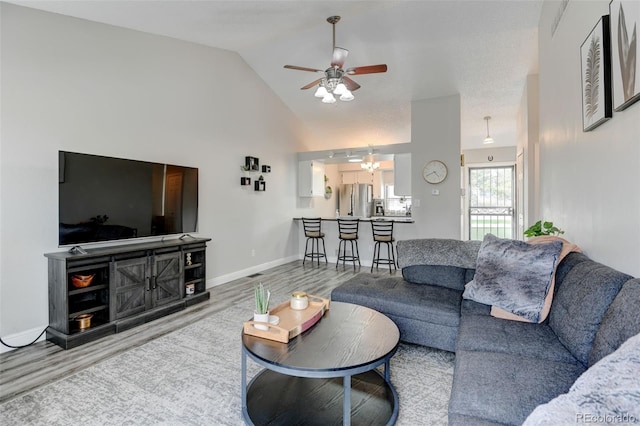 living area with baseboards, ceiling fan with notable chandelier, wood finished floors, and vaulted ceiling