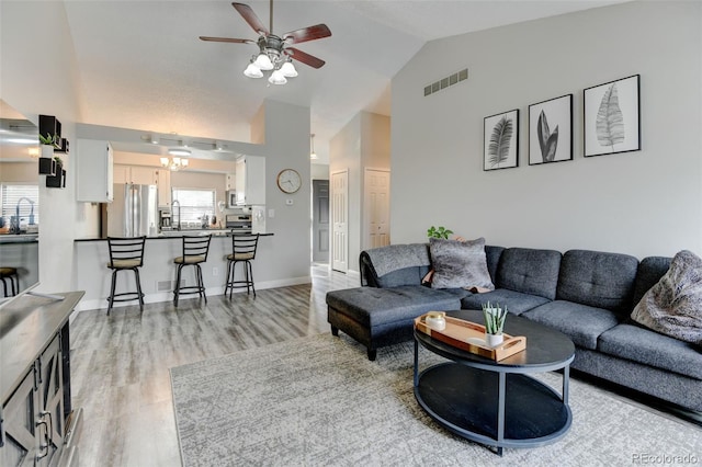 living room featuring ceiling fan, light wood finished floors, high vaulted ceiling, baseboards, and visible vents