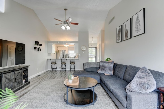 living area with ceiling fan, visible vents, wood finished floors, baseboards, and high vaulted ceiling