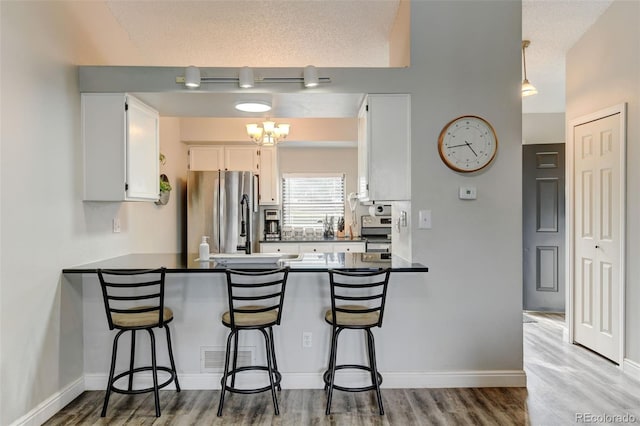 kitchen featuring dark countertops, appliances with stainless steel finishes, a peninsula, white cabinetry, and wood finished floors