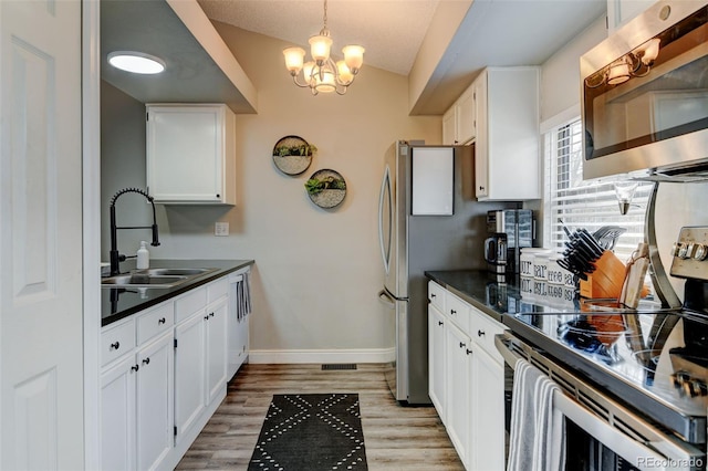 kitchen with white cabinets, dark countertops, appliances with stainless steel finishes, a sink, and baseboards