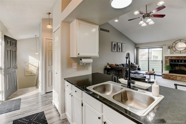 kitchen featuring visible vents, dark countertops, vaulted ceiling, a sink, and open floor plan