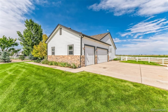 view of side of property with fence, driveway, a yard, stone siding, and an attached garage