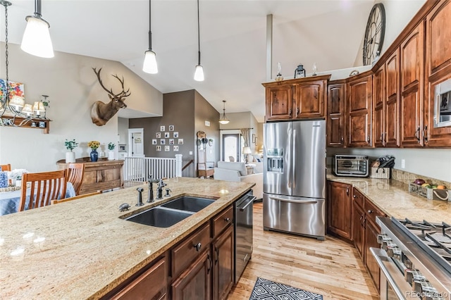 kitchen featuring a sink, light stone counters, stainless steel appliances, light wood-style floors, and hanging light fixtures