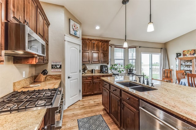 kitchen featuring light stone counters, light wood finished floors, a sink, vaulted ceiling, and appliances with stainless steel finishes