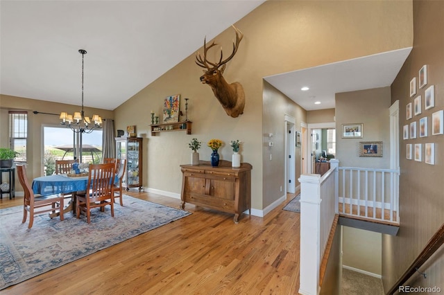 dining area featuring baseboards, light wood-style floors, an inviting chandelier, and high vaulted ceiling