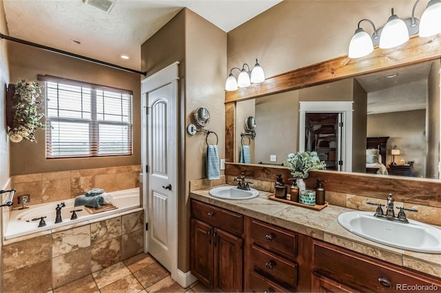 bathroom with double vanity, a bath, visible vents, and a sink