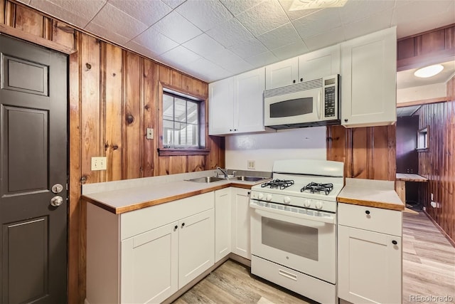 kitchen with white cabinets, wood walls, white appliances, and sink