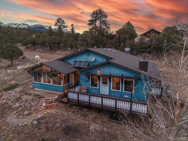 rustic home with a mountain view, roof with shingles, and a sunroom