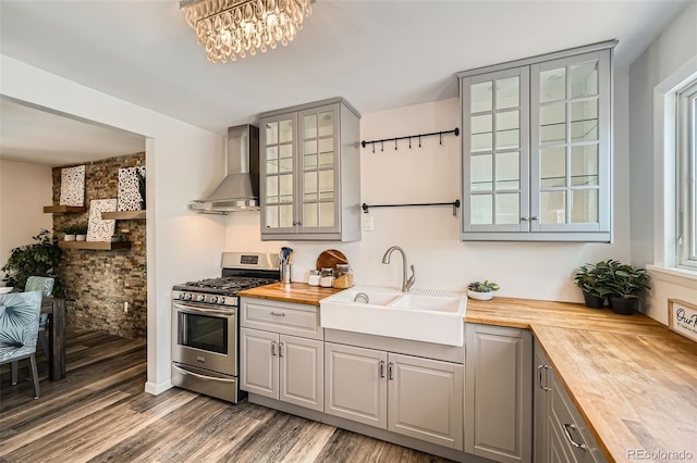 kitchen featuring butcher block countertops, stainless steel gas range oven, wall chimney range hood, gray cabinetry, and a sink