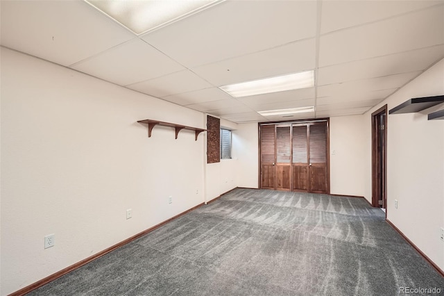 basement featuring a drop ceiling, carpet flooring, and baseboards