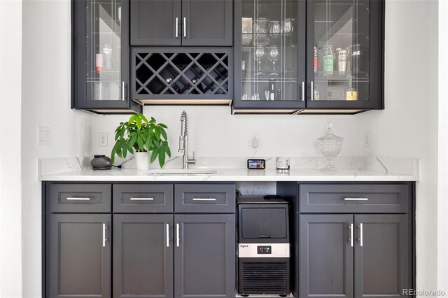 bar featuring gray cabinets, light stone counters, and sink