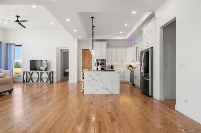 kitchen with light wood-type flooring, appliances with stainless steel finishes, backsplash, light stone counters, and ceiling fan