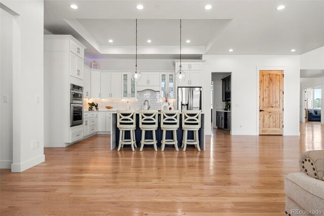 kitchen featuring an island with sink, light wood-type flooring, stainless steel appliances, and hanging light fixtures