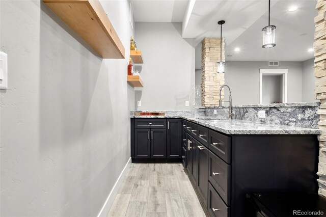 kitchen featuring pendant lighting, light stone countertops, sink, light hardwood / wood-style floors, and kitchen peninsula