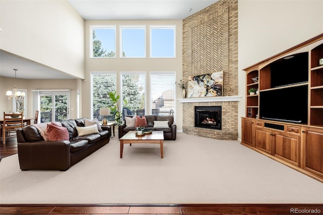 living area featuring a healthy amount of sunlight, a brick fireplace, an inviting chandelier, and a towering ceiling