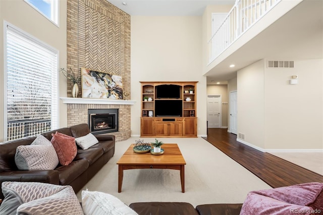 living area featuring visible vents, a brick fireplace, baseboards, a towering ceiling, and wood finished floors