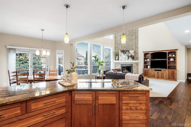 kitchen with dark wood-style floors, brown cabinetry, stone counters, black electric stovetop, and a brick fireplace