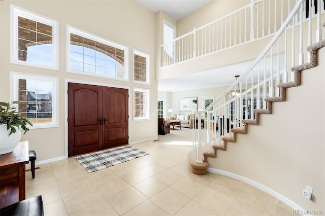 entrance foyer featuring stairway, baseboards, a towering ceiling, and tile patterned flooring