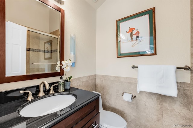 bathroom with a wainscoted wall, toilet, a stall shower, tile walls, and vanity