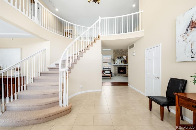 tiled entrance foyer featuring visible vents, a large fireplace, baseboards, stairs, and a towering ceiling