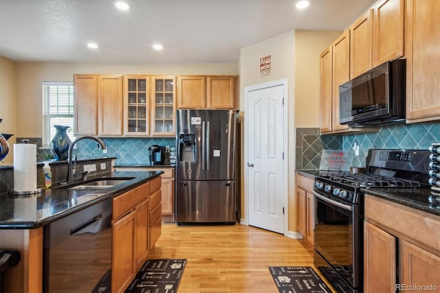 kitchen with tasteful backsplash, dark stone counters, sink, black appliances, and light hardwood / wood-style flooring