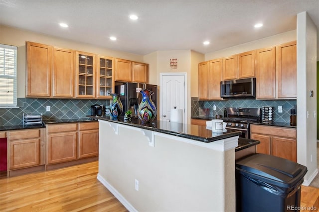 kitchen featuring backsplash, stainless steel appliances, light hardwood / wood-style flooring, a kitchen island, and a breakfast bar area