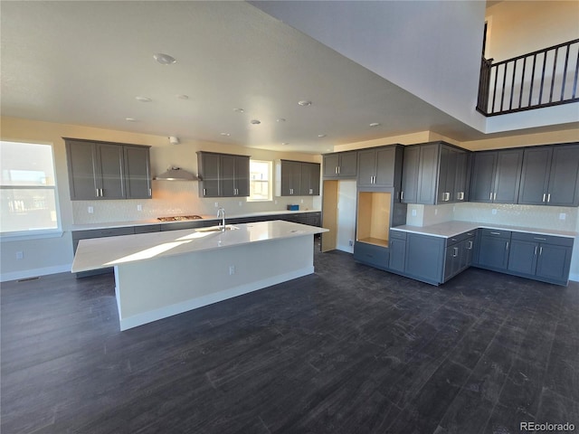 kitchen featuring dark wood finished floors, gray cabinets, light countertops, a sink, and an island with sink